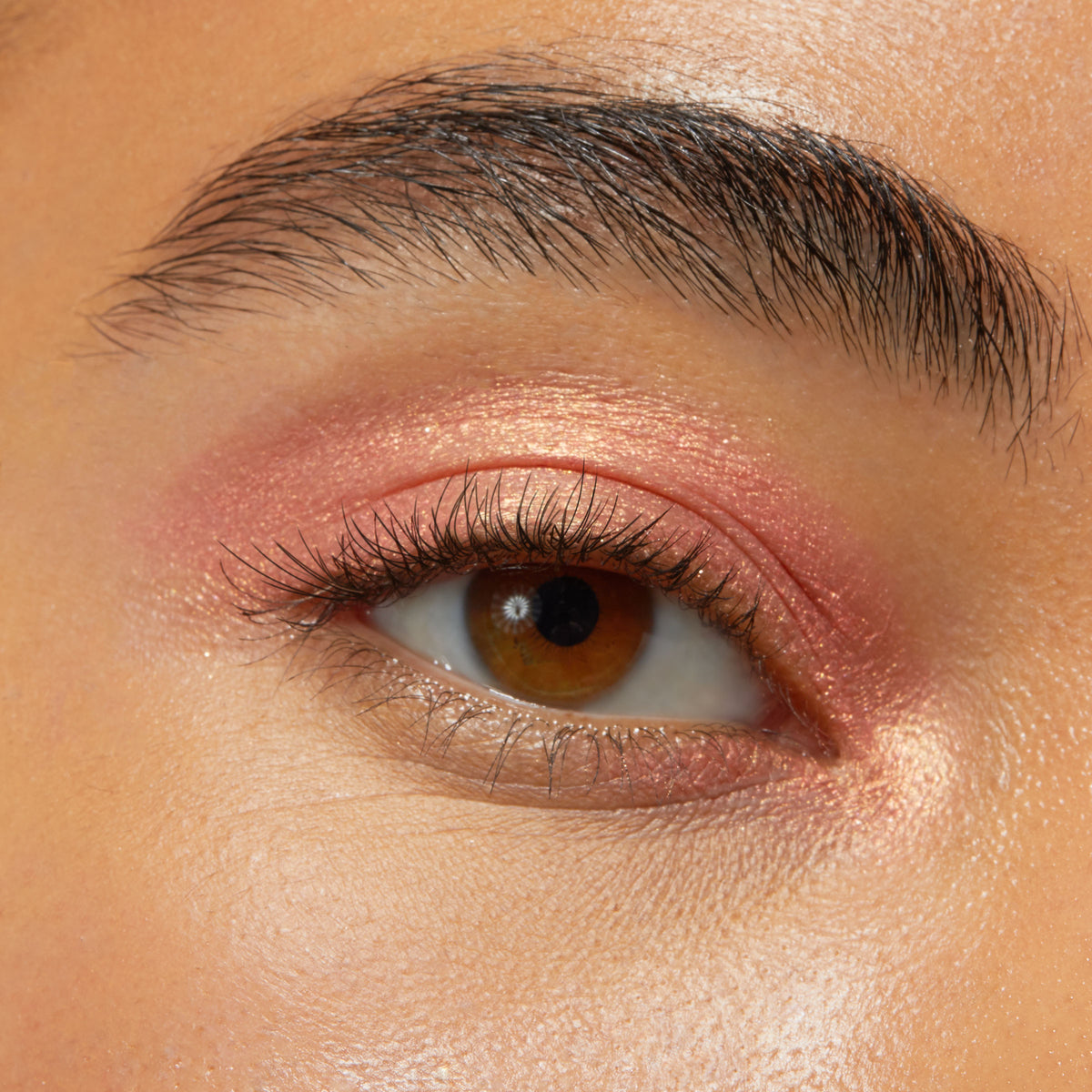 Brown eye wearing Friday Feels Shadow Stix, a shimmering rose-gold pink from the ColourPop Shadow Stix line, swept across the lid and inner corner with a soft metallic sheen in a close-up beauty swatch.